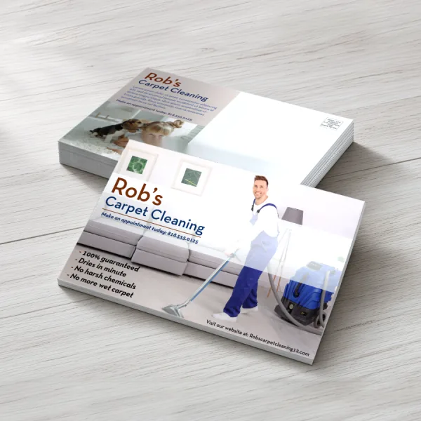 Stack of custom Rob's Carpet Cleaning postcards showing the photo front and the white mailing side on light wood.