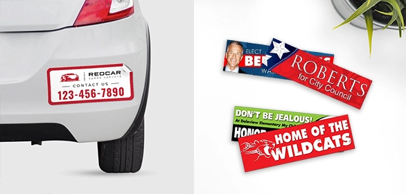 White car bumper with rectangular auto service magnet and three colorful political and sports bumper stickers.
