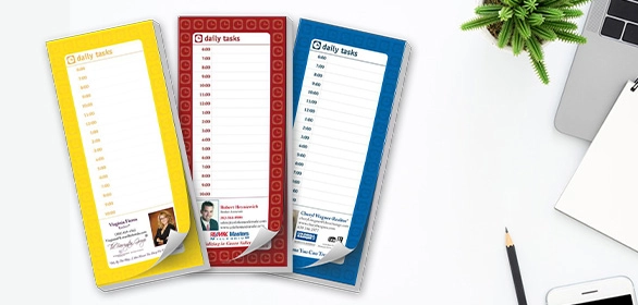 Three vertical daily task list notepads in yellow, red, and blue with portrait photos beside a pencil and laptop edge.