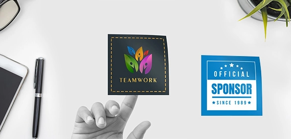 Two square magnets with teamwork floral design and blue sponsor badge on desk near phone, pen, and plant.