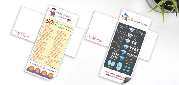 Two tall narrow notepads with colorful daycare and baby-themed designs on a white desk with a plant.