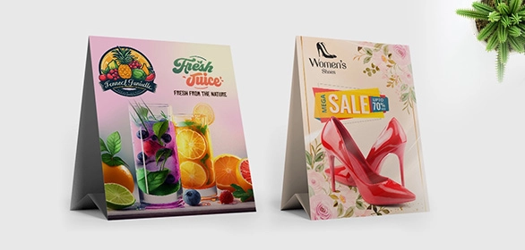 Two tent-style table cards showing fresh juice drinks with fruit and a red high-heeled shoe with floral sale design.