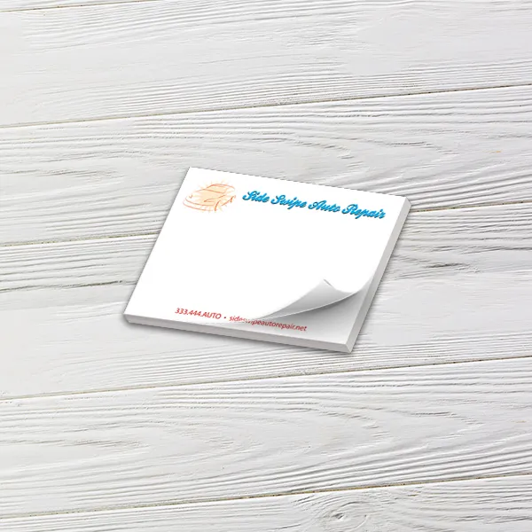 Custom 4 x 3 inch landscape memo pad with a script auto repair logo, top sheet curling, on white wood