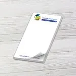 Custom 4 x 7 inch memo pad with a graduation cap logo, top sheet curling, on white wood