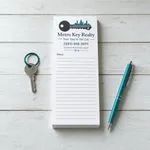 Custom 3.5x8 real estate notepad with a teal city skyline and key logo, a teal key ring and a matching pen on a wood table