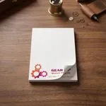 Custom 3 x 4 inch watch repair memo pad, top sheet curling, on a desk with tiny gears and tools