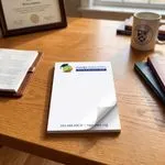 Custom 4 x 7 inch higher education memo pad, top sheet curling, on a desk with a framed diploma and a mug
