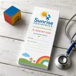 Custom 3 x 8 inch pediatric clinic notepad with rainbow, phone and Next Visit lines, beside a toy block and stethoscope